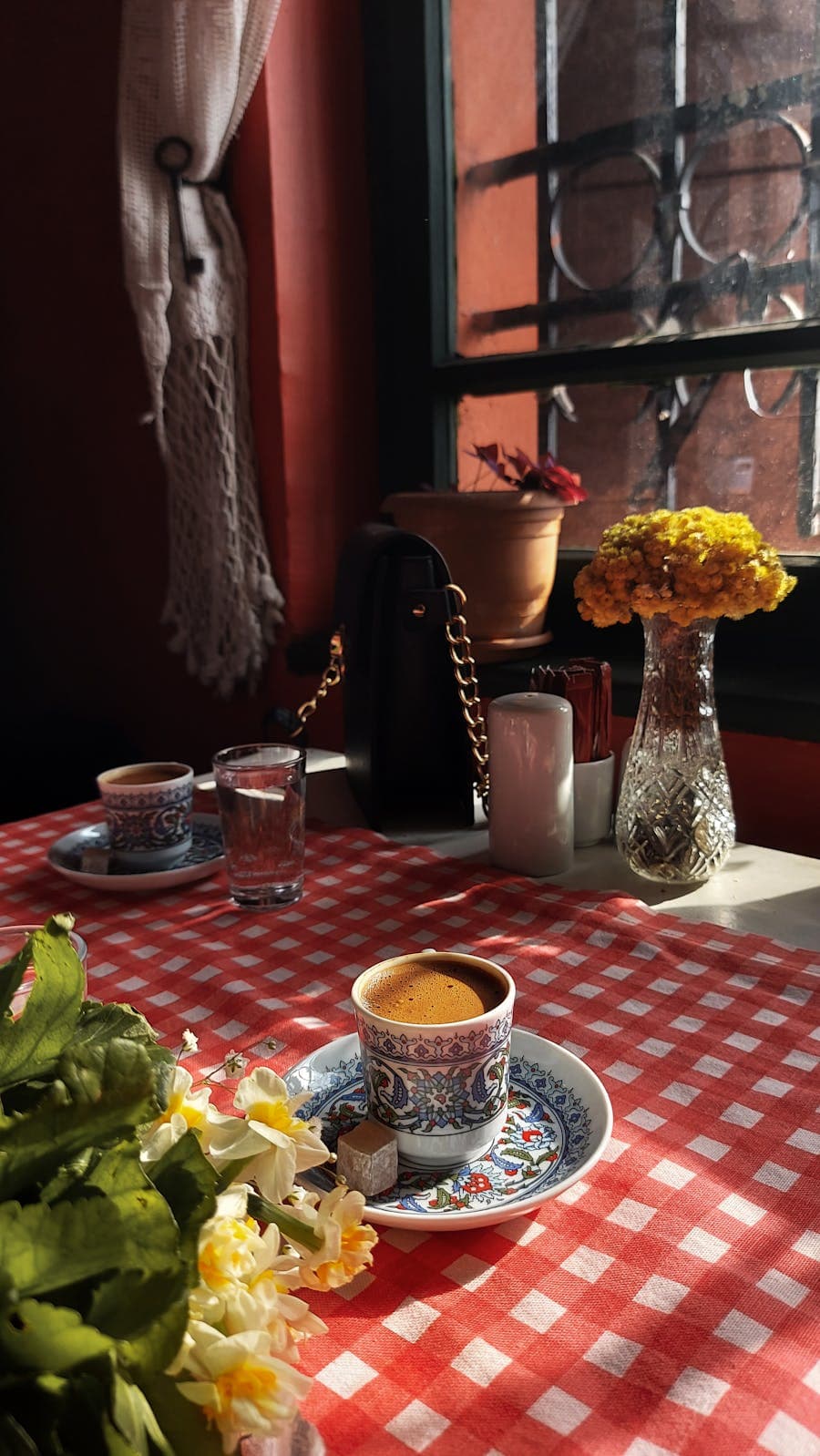Sunlit corner table with linen tablecloth and a single stem in a glass bottle.