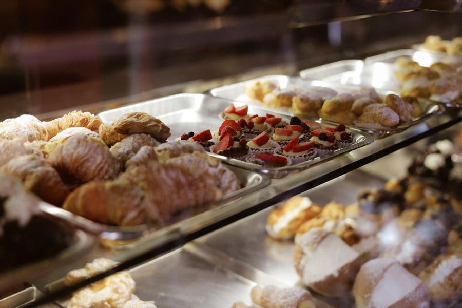 Glass pastry case with croissants, tarts, and cakes on ceramic stands.