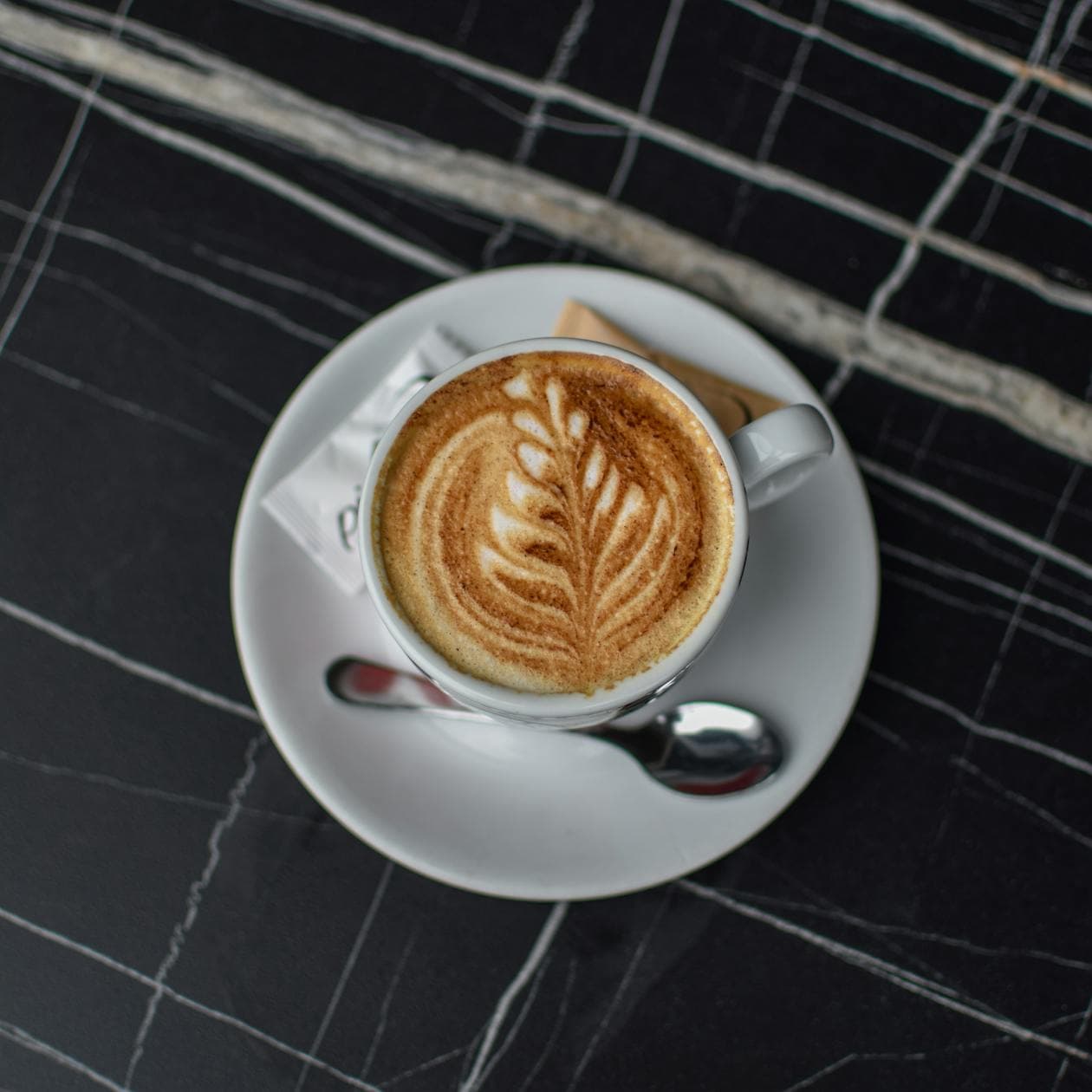 Cappuccino with intricate latte art served on a dark marble table at Aurelia Café — photo by Jovan Popović